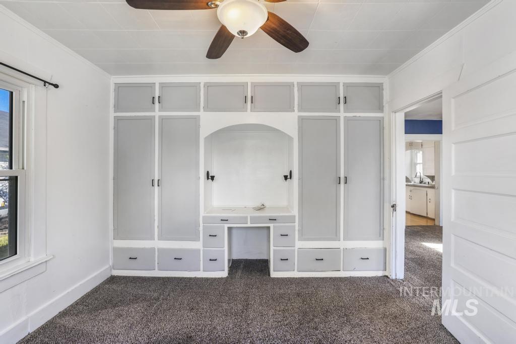 Unfurnished bedroom with dark carpet, crown molding, ceiling fan, and a closet