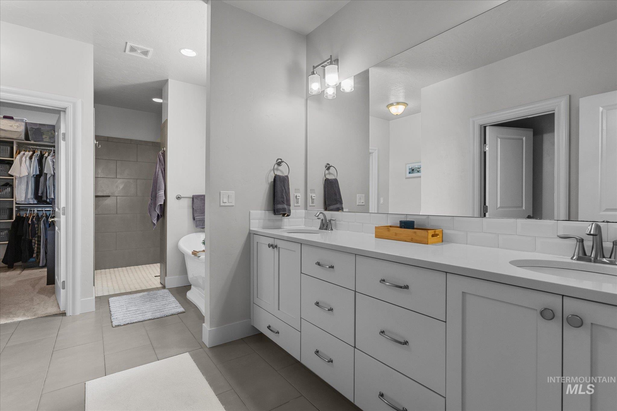 Bathroom with double vanity, tile patterned floors, tiled shower, a spacious closet, and a soaking tub