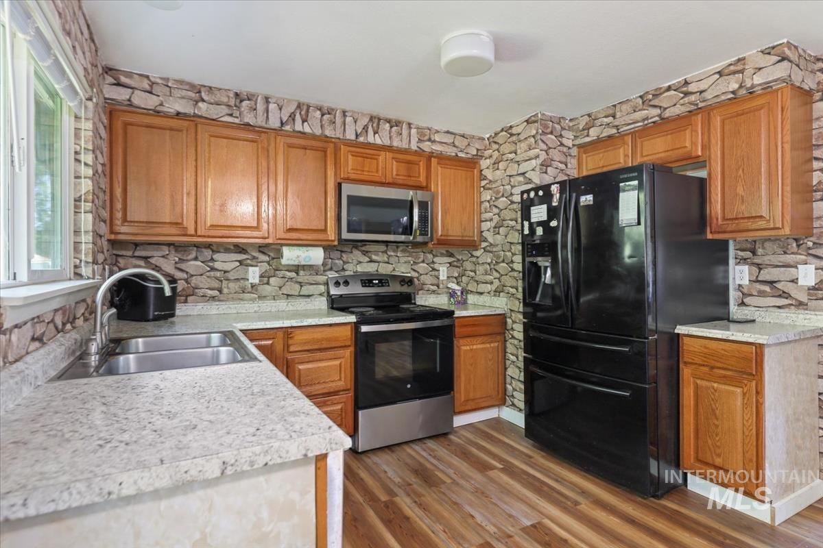 Kitchen featuring stainless steel appliances, light countertops, brown cabinetry, and dark wood-style flooring