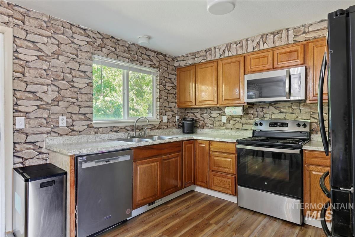 Kitchen with appliances with stainless steel finishes, brown cabinets, dark wood-style flooring, and light stone countertops