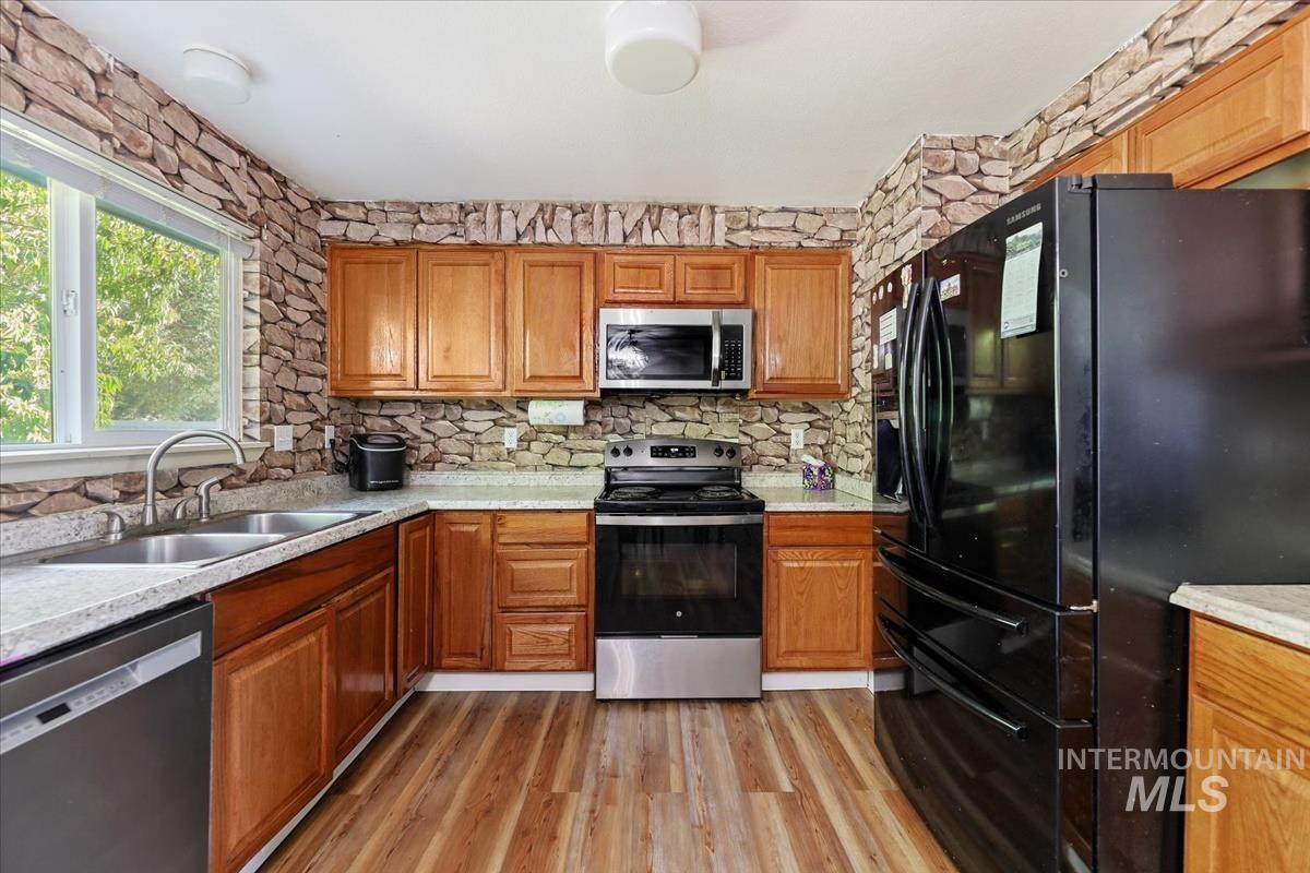 Kitchen featuring appliances with stainless steel finishes, brown cabinets, light wood finished floors, and light stone countertops
