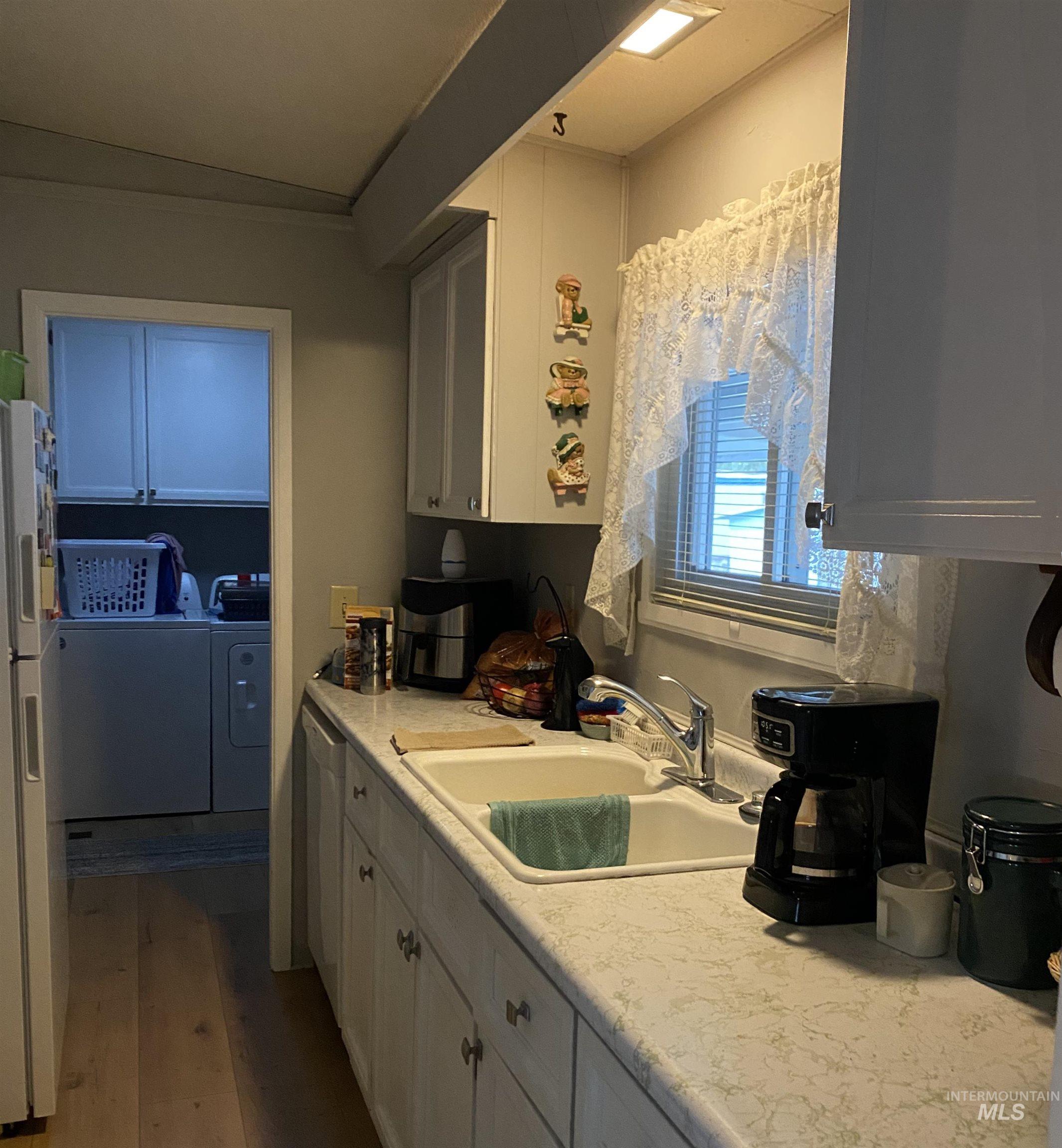 Kitchen featuring independent washer and dryer, white cabinetry, light countertops, dark wood-type flooring, and white appliances
