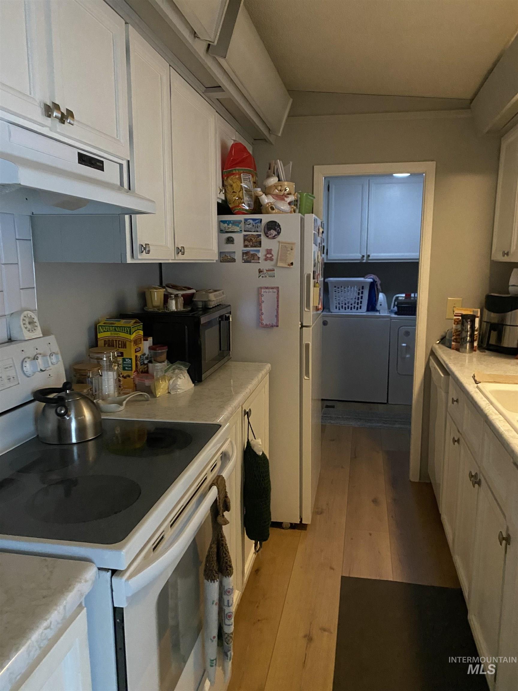 Kitchen featuring white appliances, white cabinets, light countertops, and washing machine and dryer
