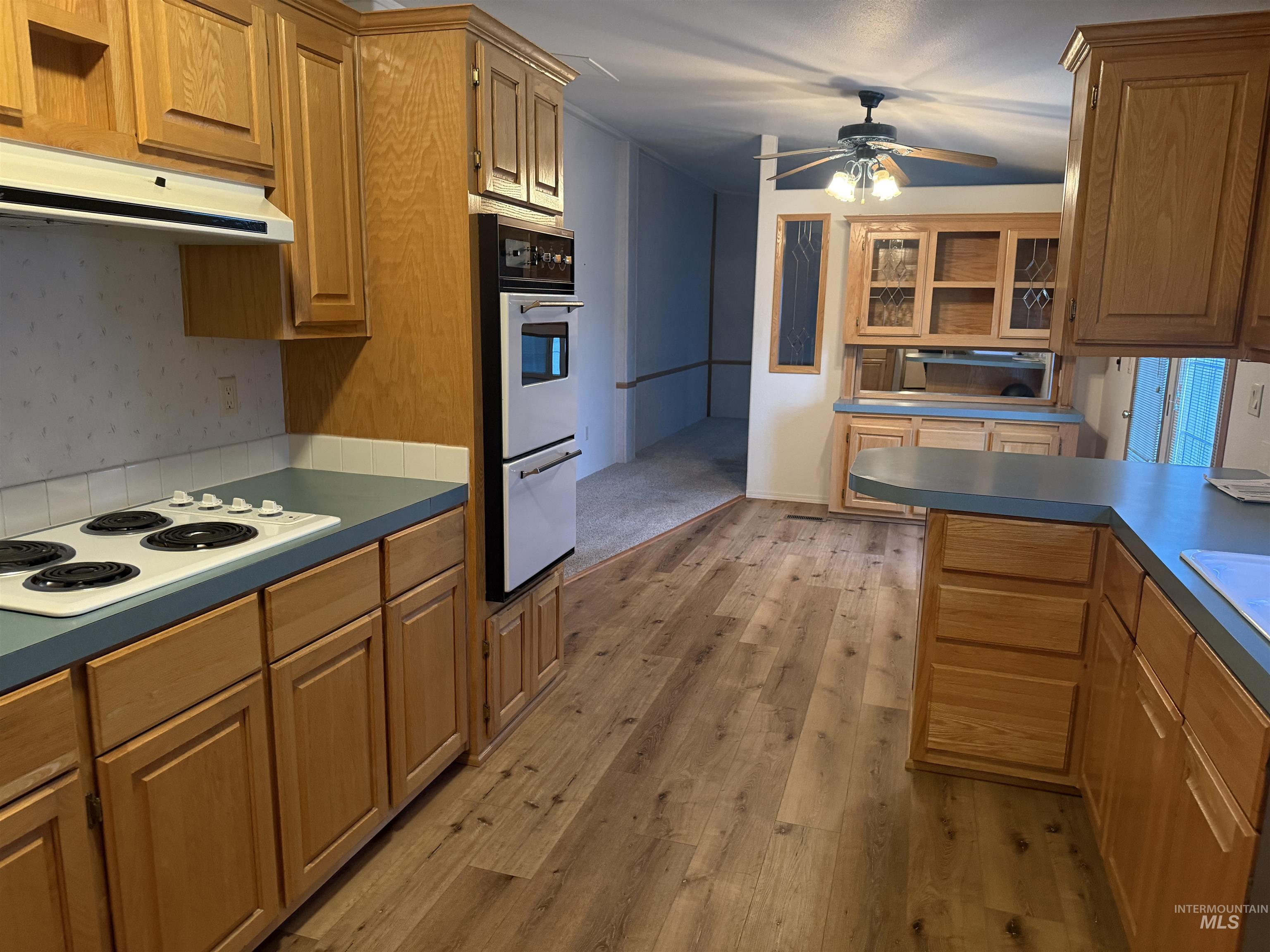 Kitchen featuring ceiling fan, white appliances, under cabinet range hood, light wood-type flooring, and brown cabinets