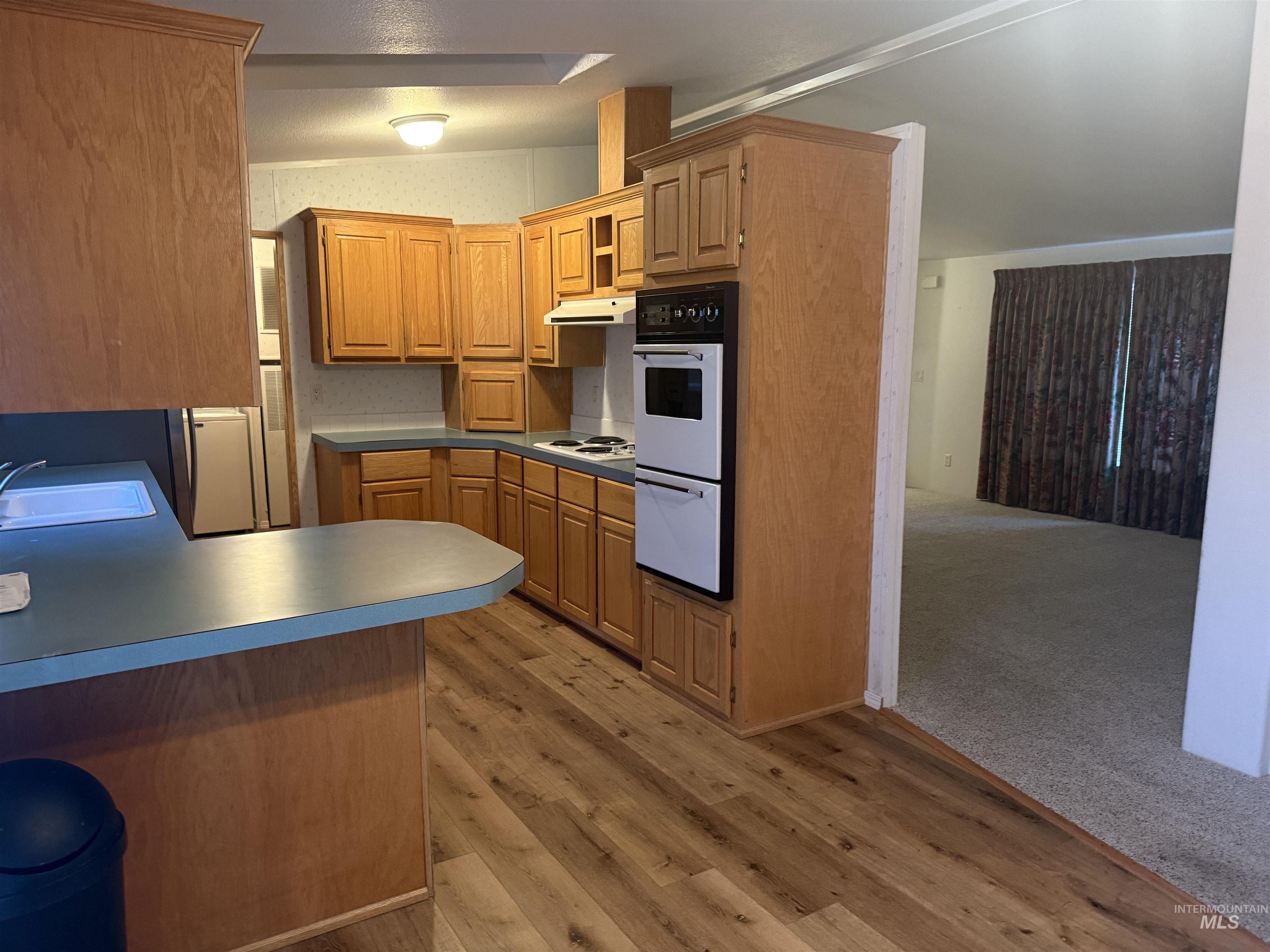 Kitchen featuring white appliances, a peninsula, light wood-style flooring, light countertops, and under cabinet range hood