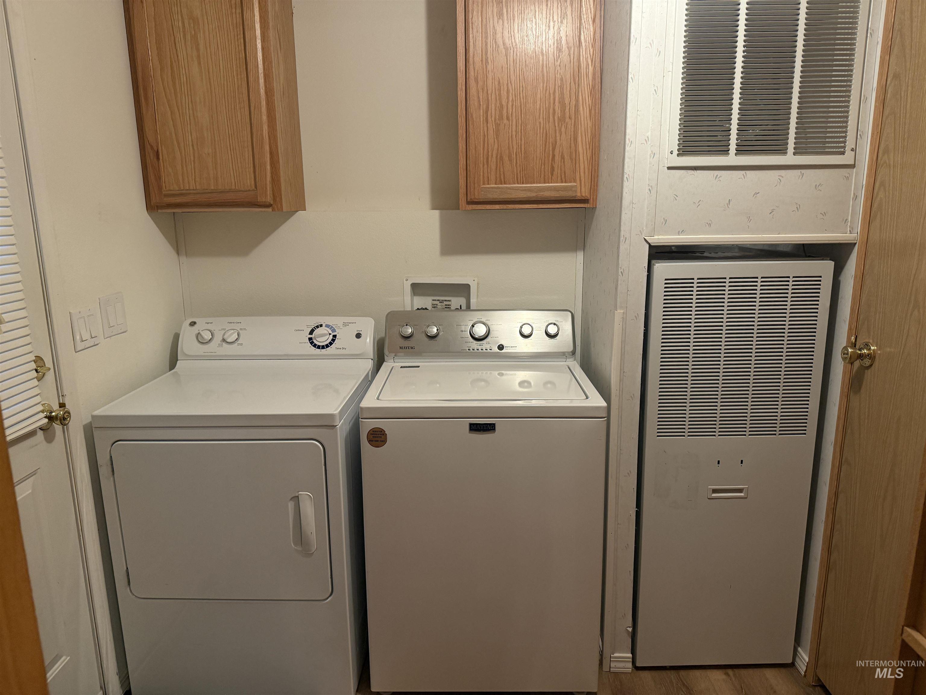 Laundry area featuring a heating unit, washing machine and dryer, wood finished floors, and cabinet space