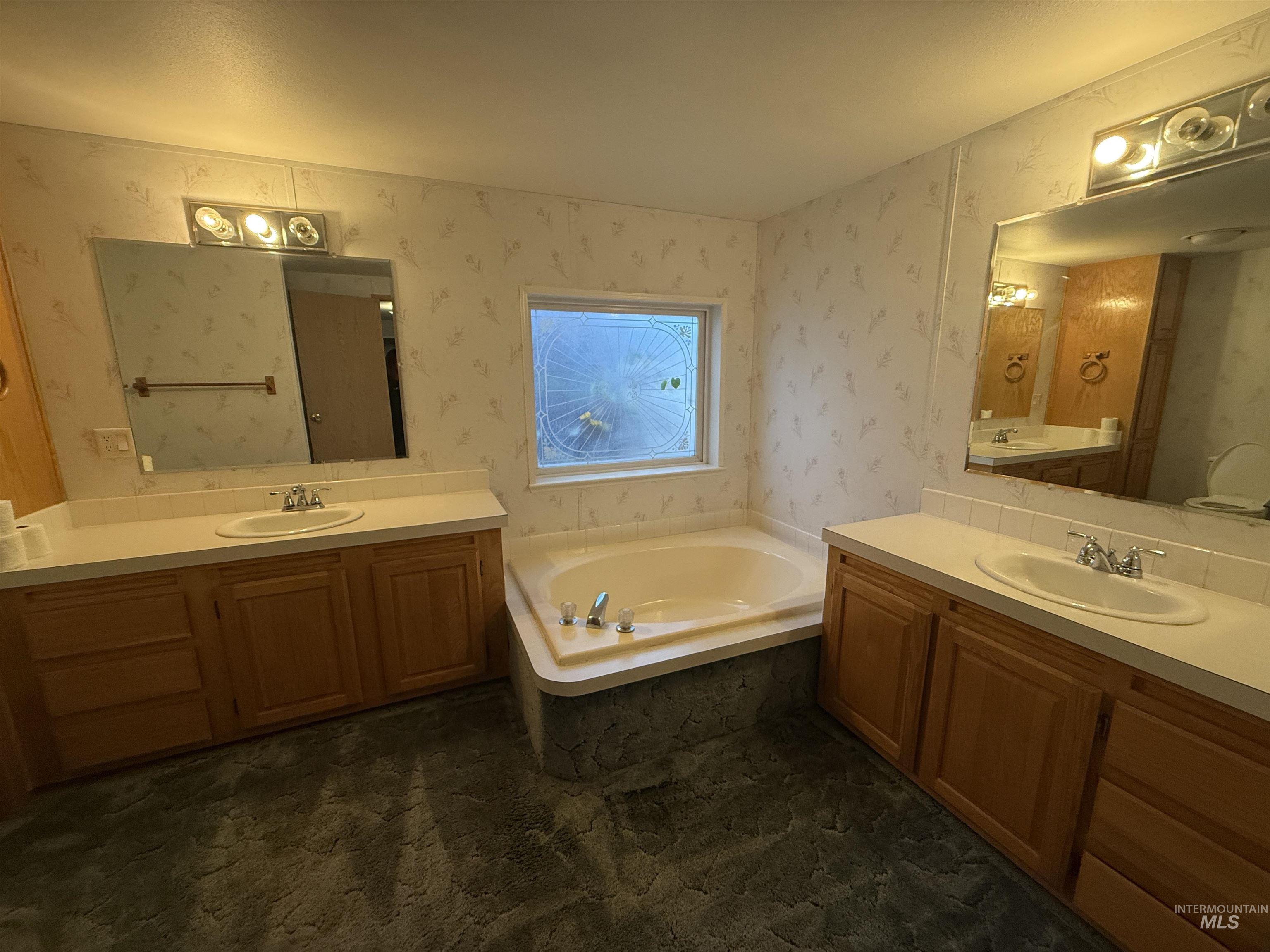 Full bath featuring two vanities, a bath, and wallpapered walls