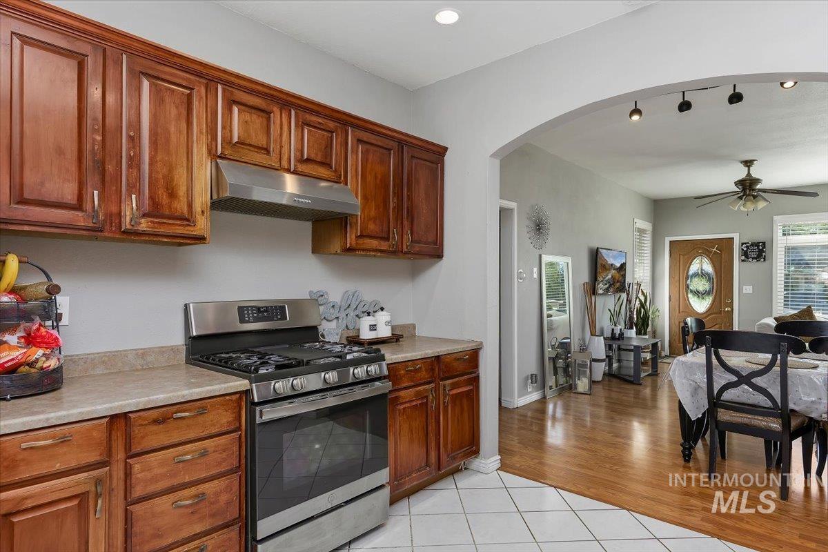 Kitchen with stainless steel range with gas stovetop, under cabinet range hood, light countertops, ceiling fan, and arched walkways