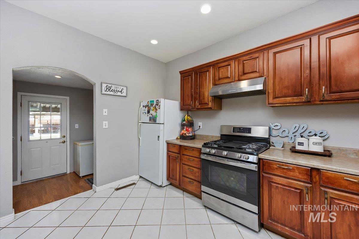 Kitchen with gas range, light countertops, under cabinet range hood, freestanding refrigerator, and light tile patterned floors