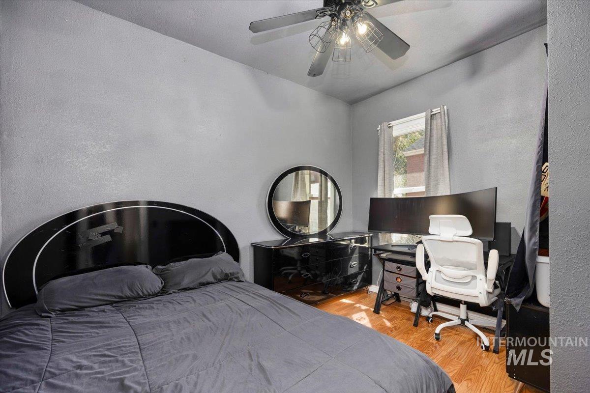 Bedroom featuring wood finished floors, a textured wall, a ceiling fan, and a desk