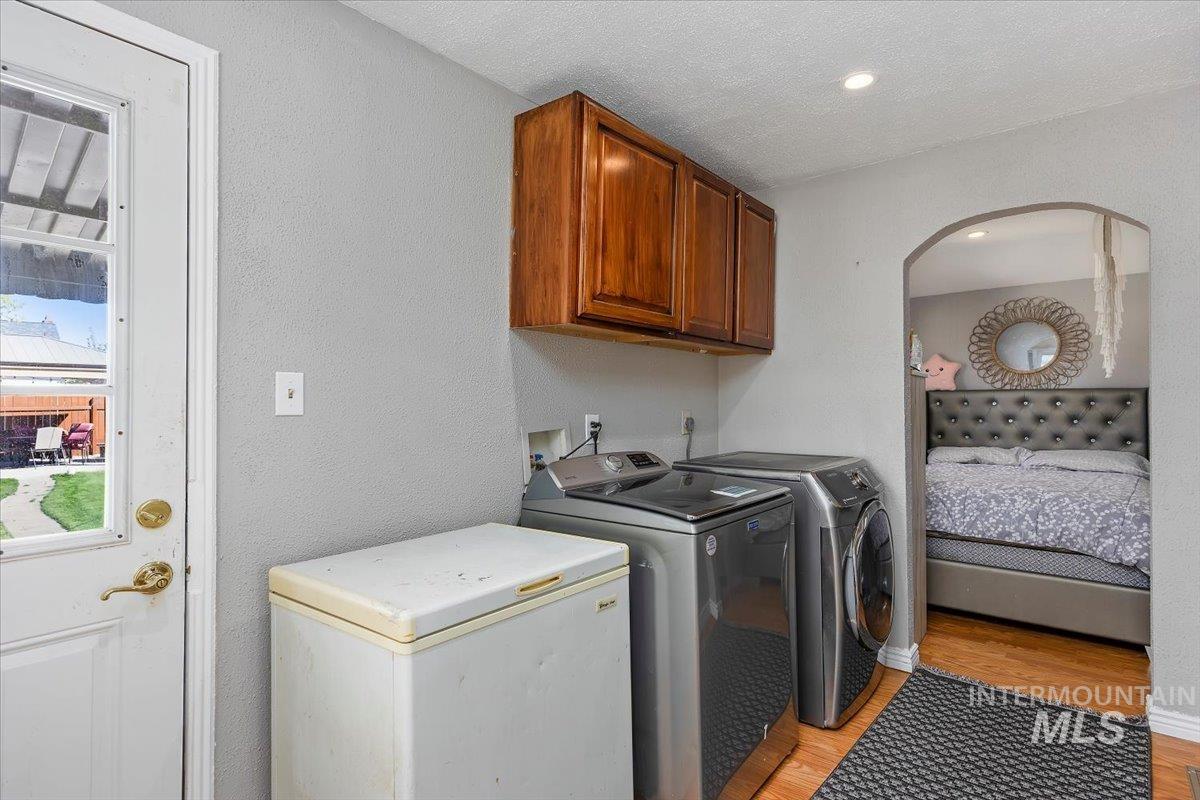 Washroom featuring light wood finished floors, cabinet space, washer and clothes dryer, and a textured wall