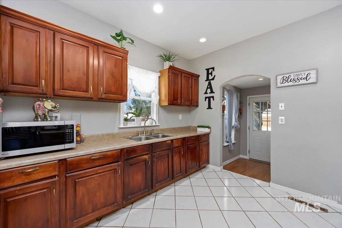 Kitchen featuring stainless steel microwave, light tile patterned floors, light countertops, arched walkways, and recessed lighting
