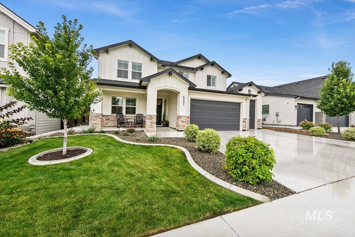 View of front of home with a porch, concrete driveway, a garage, stone siding, and a front yard