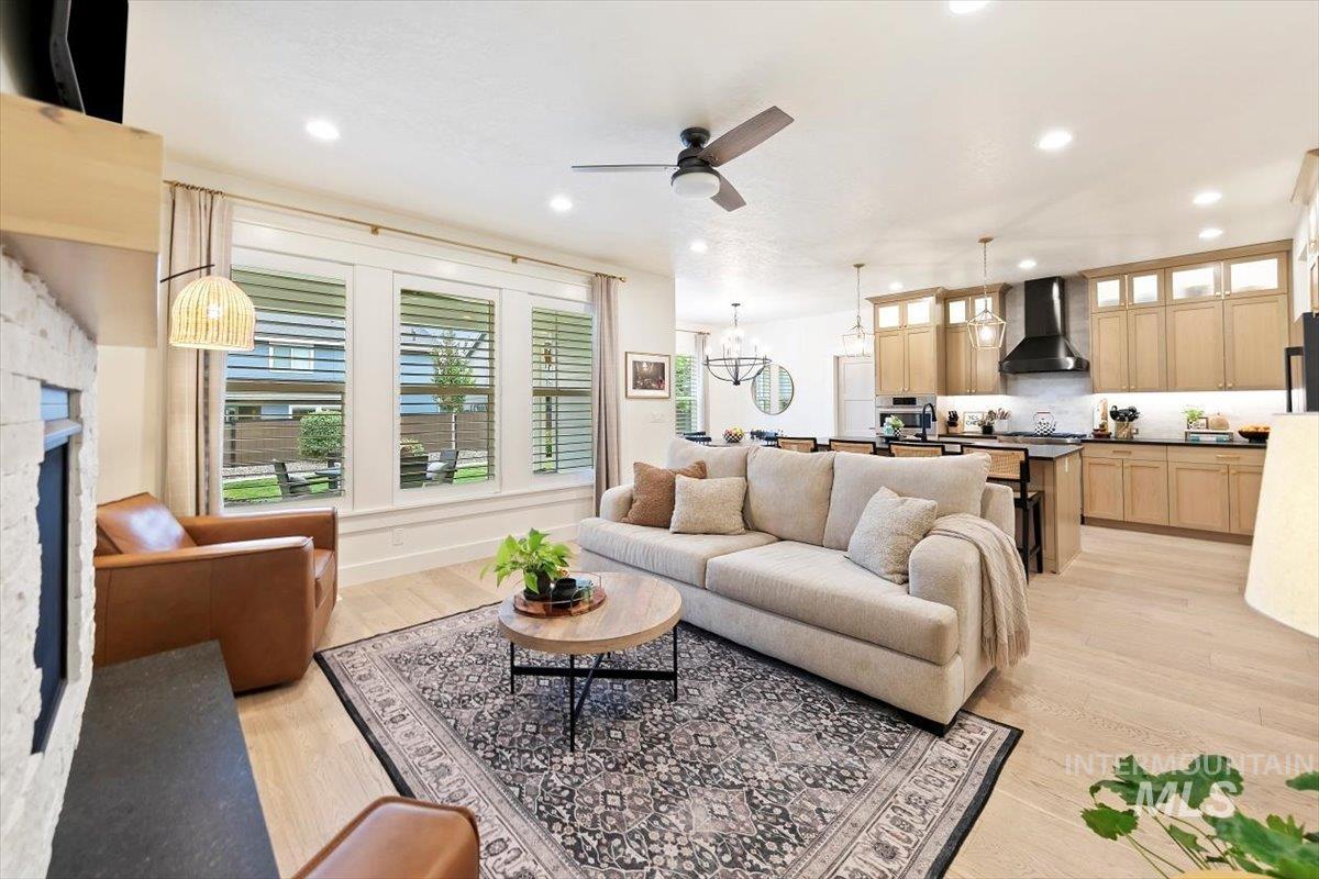Living area featuring light wood-style floors, ceiling fan, recessed lighting, a fireplace, and a chandelier