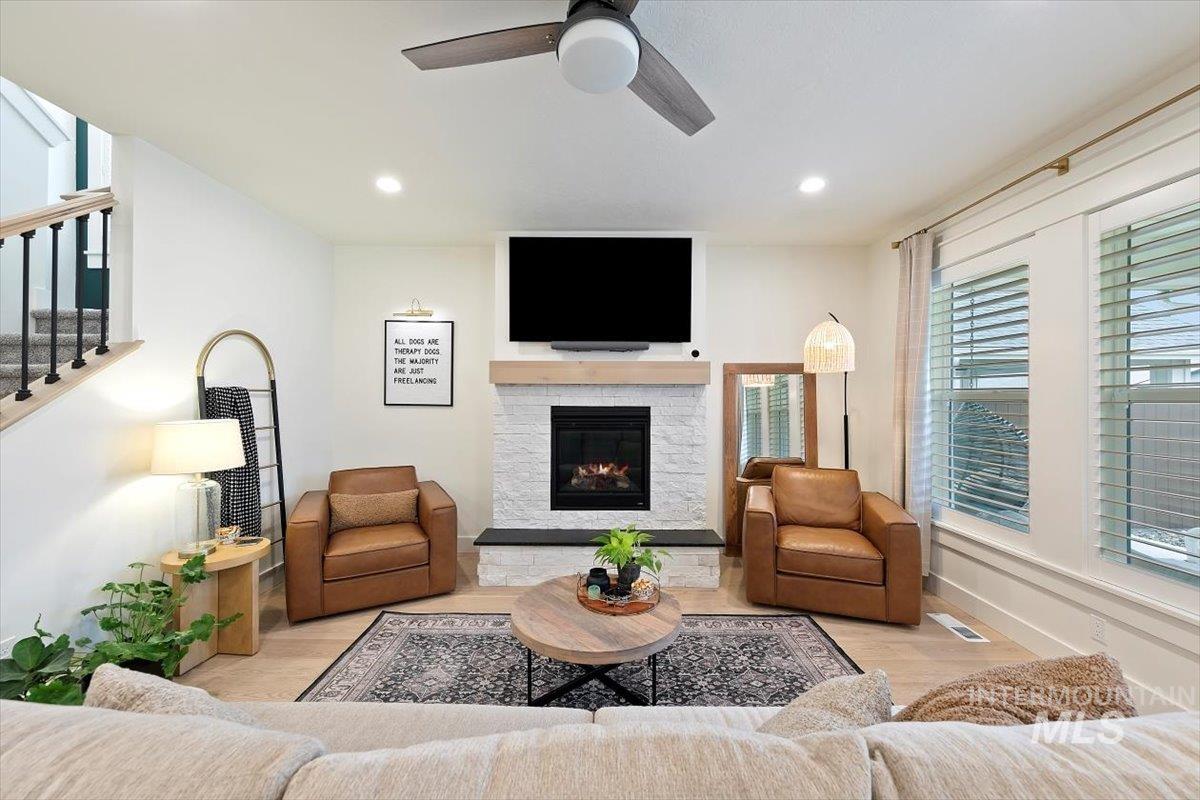 Living room with wood finished floors, recessed lighting, a fireplace, a ceiling fan, and stairs