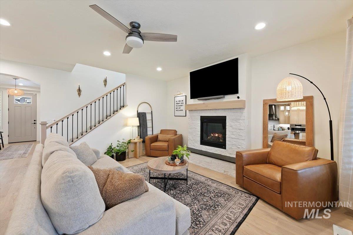 Living room featuring light wood-style flooring, recessed lighting, ceiling fan, stairway, and a fireplace
