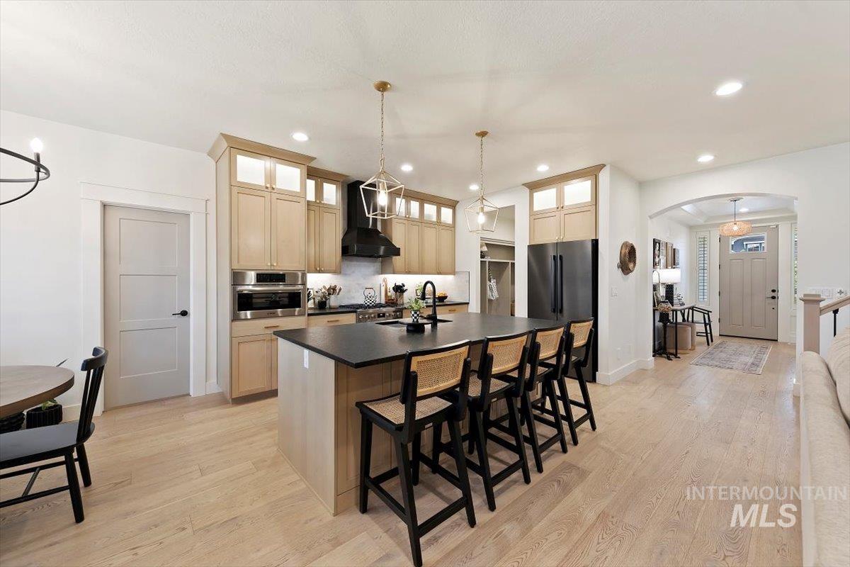 Kitchen featuring a center island with sink, arched walkways, a kitchen breakfast bar, dark countertops, and wall chimney range hood