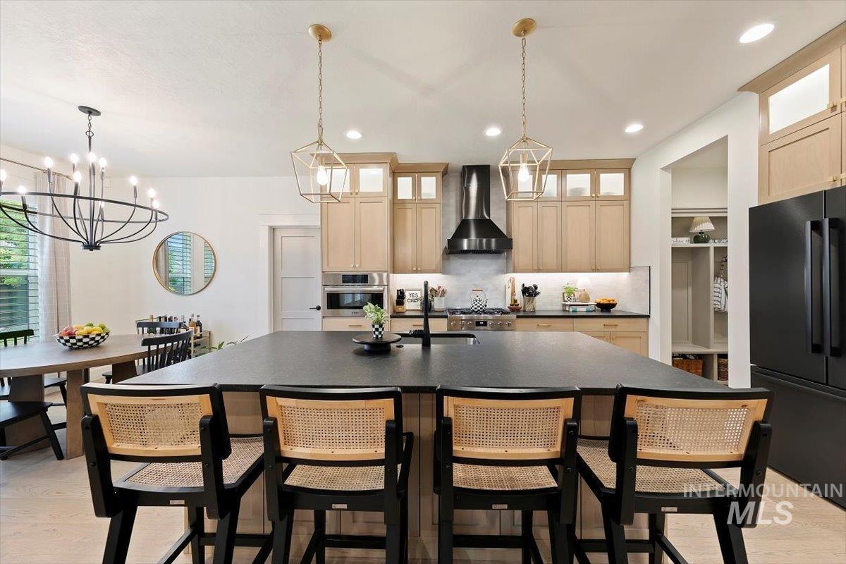 Kitchen with light wood-style floors, freestanding refrigerator, pendant lighting, wall chimney range hood, and recessed lighting
