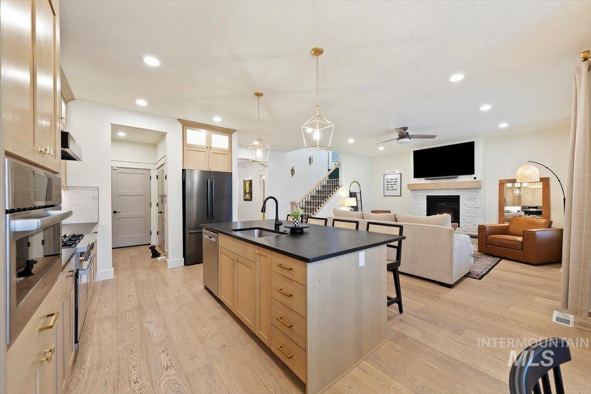 Kitchen featuring an island with sink, a lit fireplace, open floor plan, light brown cabinetry, and hanging light fixtures