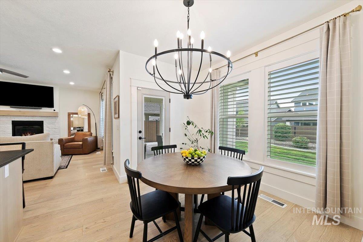 Dining space featuring a lit fireplace, light wood-style flooring, recessed lighting, and a chandelier