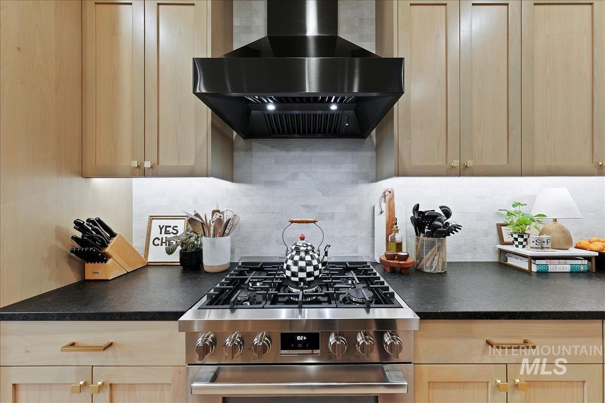 Kitchen with dark countertops, extractor fan, gas stove, and backsplash