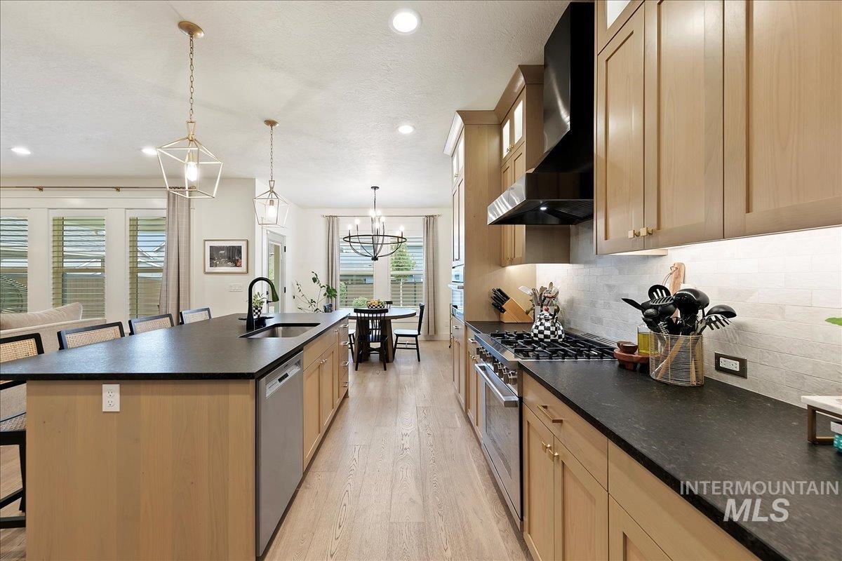 Kitchen with a breakfast bar, light wood-style floors, wall chimney range hood, an island with sink, and stainless steel appliances
