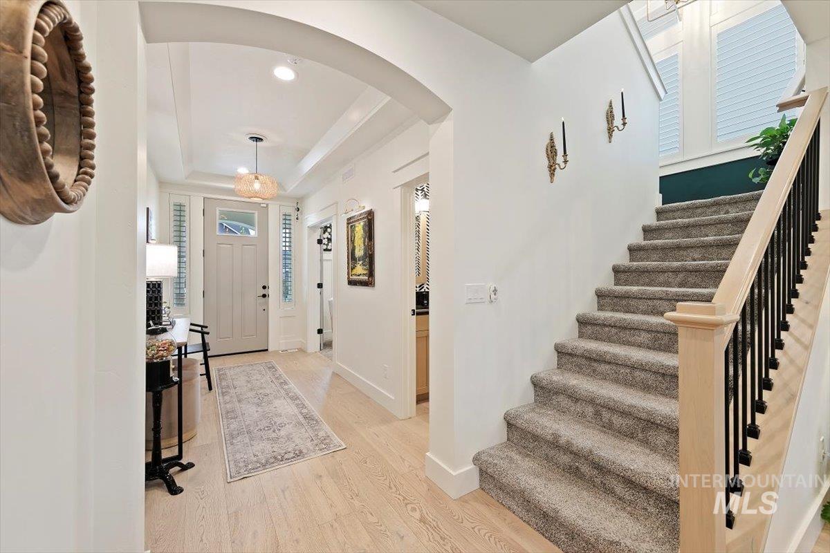 Entrance foyer with arched walkways, light wood finished floors, a raised ceiling, stairs, and recessed lighting