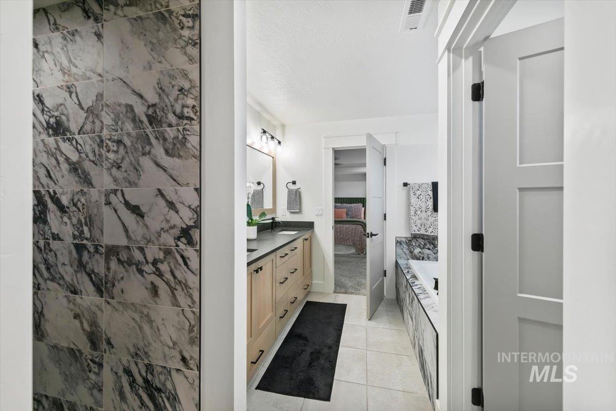 Bathroom featuring double vanity, connected bathroom, a bath, light tile patterned floors, and a textured ceiling