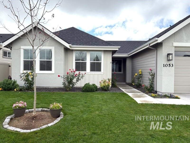 Ranch-style home featuring a front yard, an attached garage, roof with shingles, and board and batten siding
