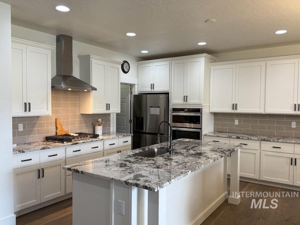 Kitchen with wall chimney exhaust hood, white cabinets, appliances with stainless steel finishes, light stone countertops, and recessed lighting