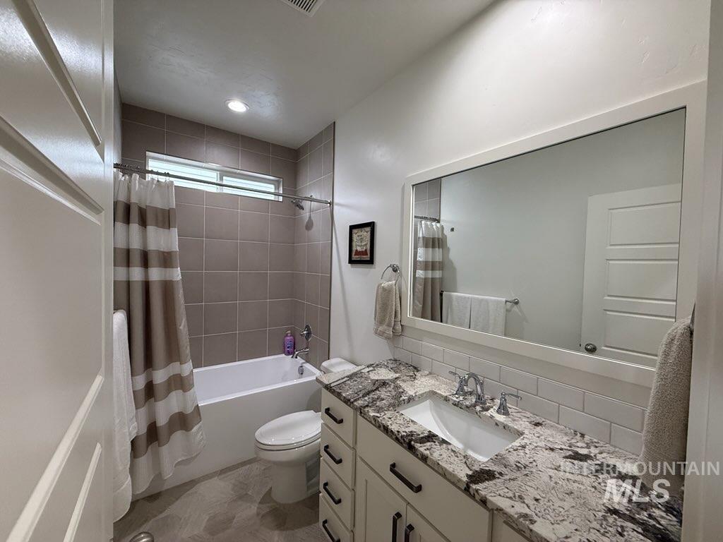 Bathroom with shower / bath combination with curtain, vanity, and decorative backsplash