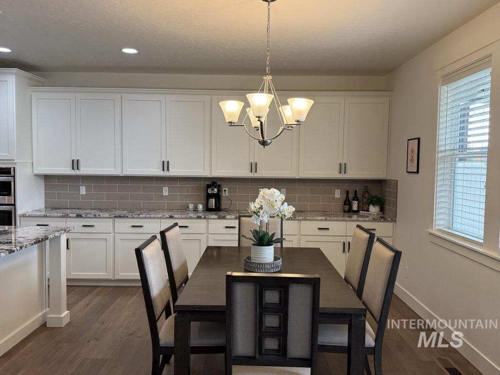 Kitchen with healthy amount of natural light, light stone counters, white cabinets, dark wood-style floors, and recessed lighting