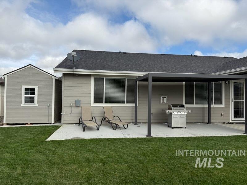 Rear view of house featuring a patio, a yard, roof with shingles, and a storage shed