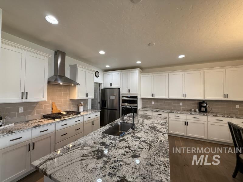 Kitchen featuring white cabinets, light stone countertops, wall chimney range hood, and recessed lighting