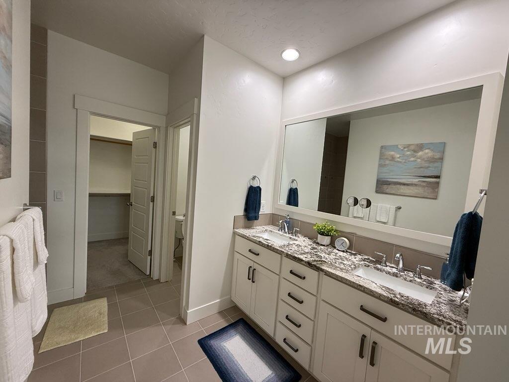 Full bath featuring double vanity, light tile patterned flooring, and a spacious closet