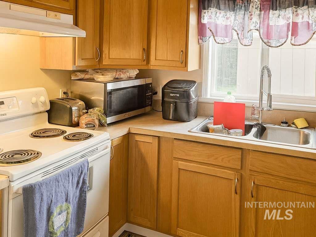 Kitchen with electric range, under cabinet range hood, light countertops, and brown cabinets