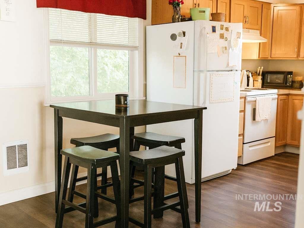 Kitchen with white appliances, under cabinet range hood, dark wood-type flooring, light countertops, and light brown cabinetry