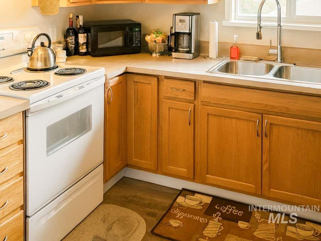 Kitchen with white range with electric cooktop, black microwave, brown cabinets, light countertops, and wood finished floors