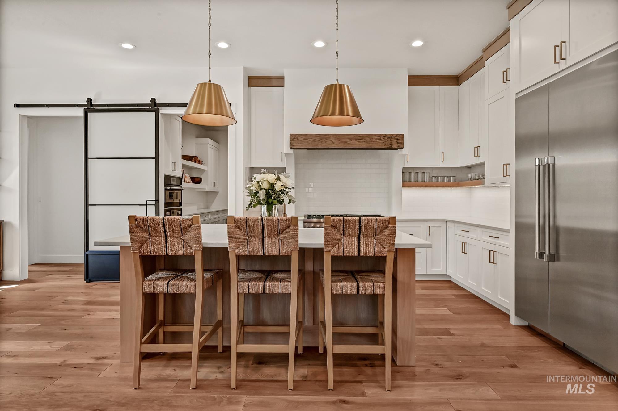 Kitchen with open shelves, a barn door, stainless steel built in fridge, decorative light fixtures, and white cabinetry