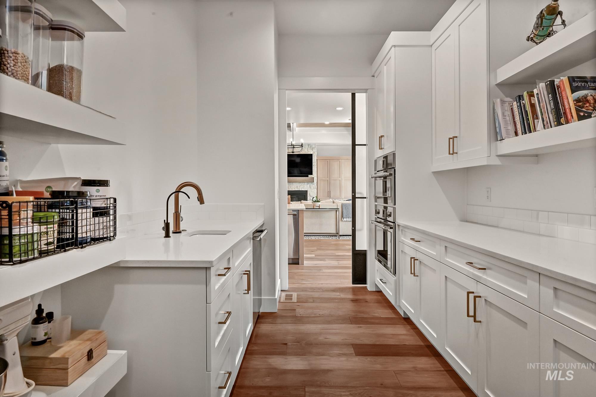 Kitchen with open shelves, white cabinetry, light wood-style floors, light stone counters, and double oven