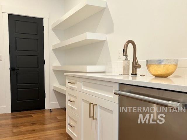 Kitchen view of dishwasher, white cabinets, and dark wood finished floors