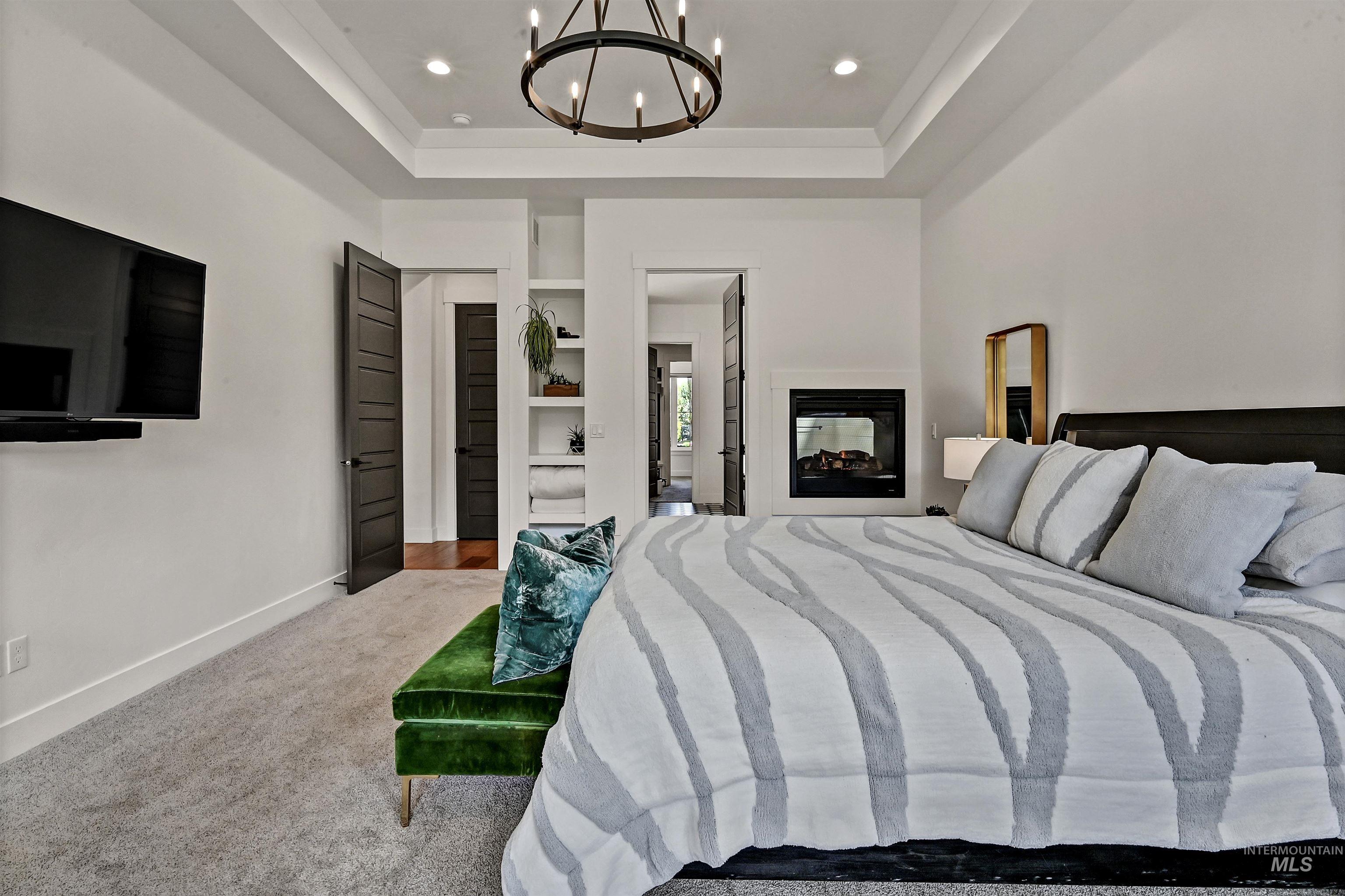 Bedroom with a chandelier, carpet floors, a tray ceiling, a multi sided fireplace, and recessed lighting
