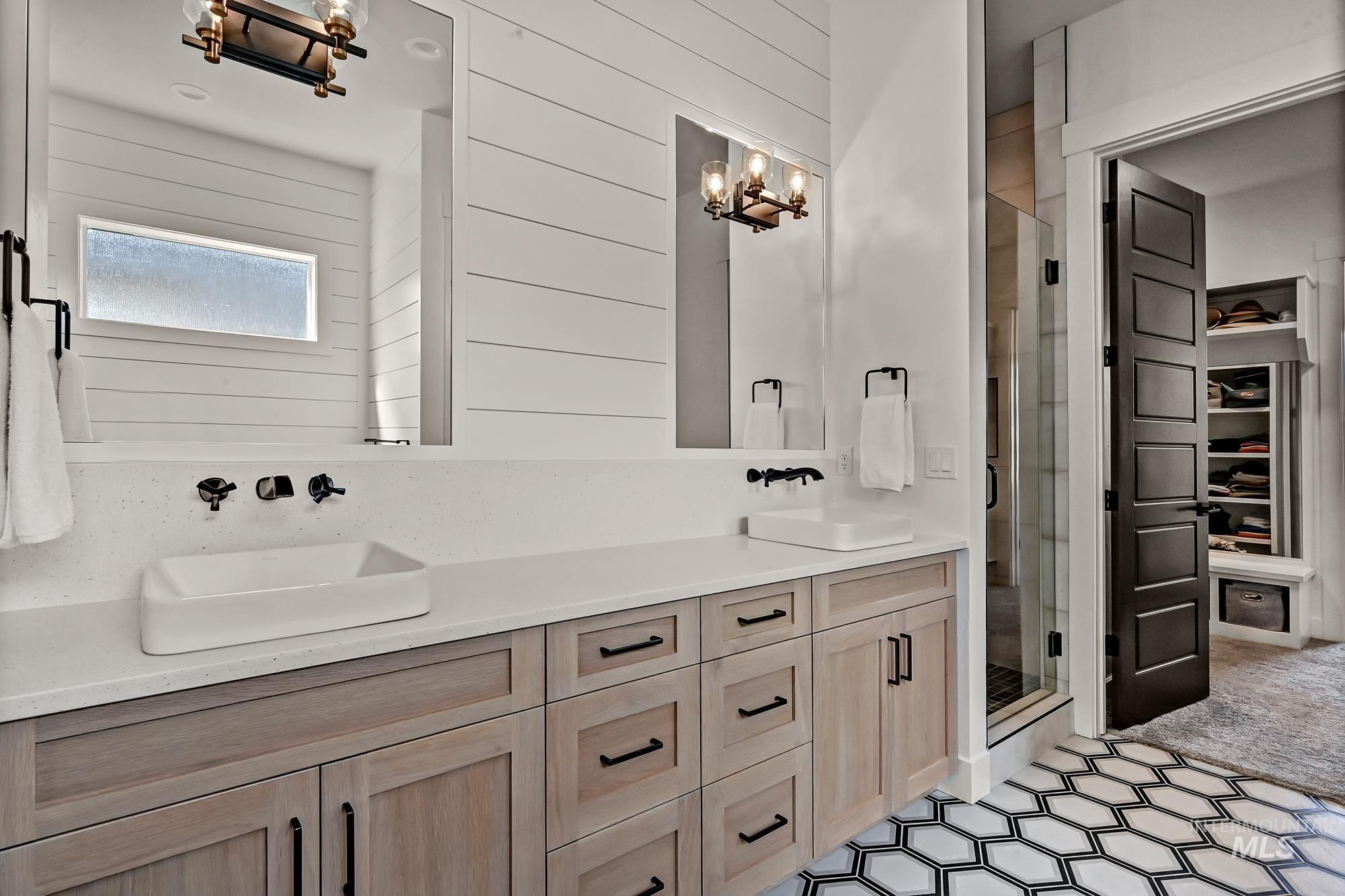 Full bath featuring double vanity, a stall shower, a spacious closet, a chandelier, and wooden walls