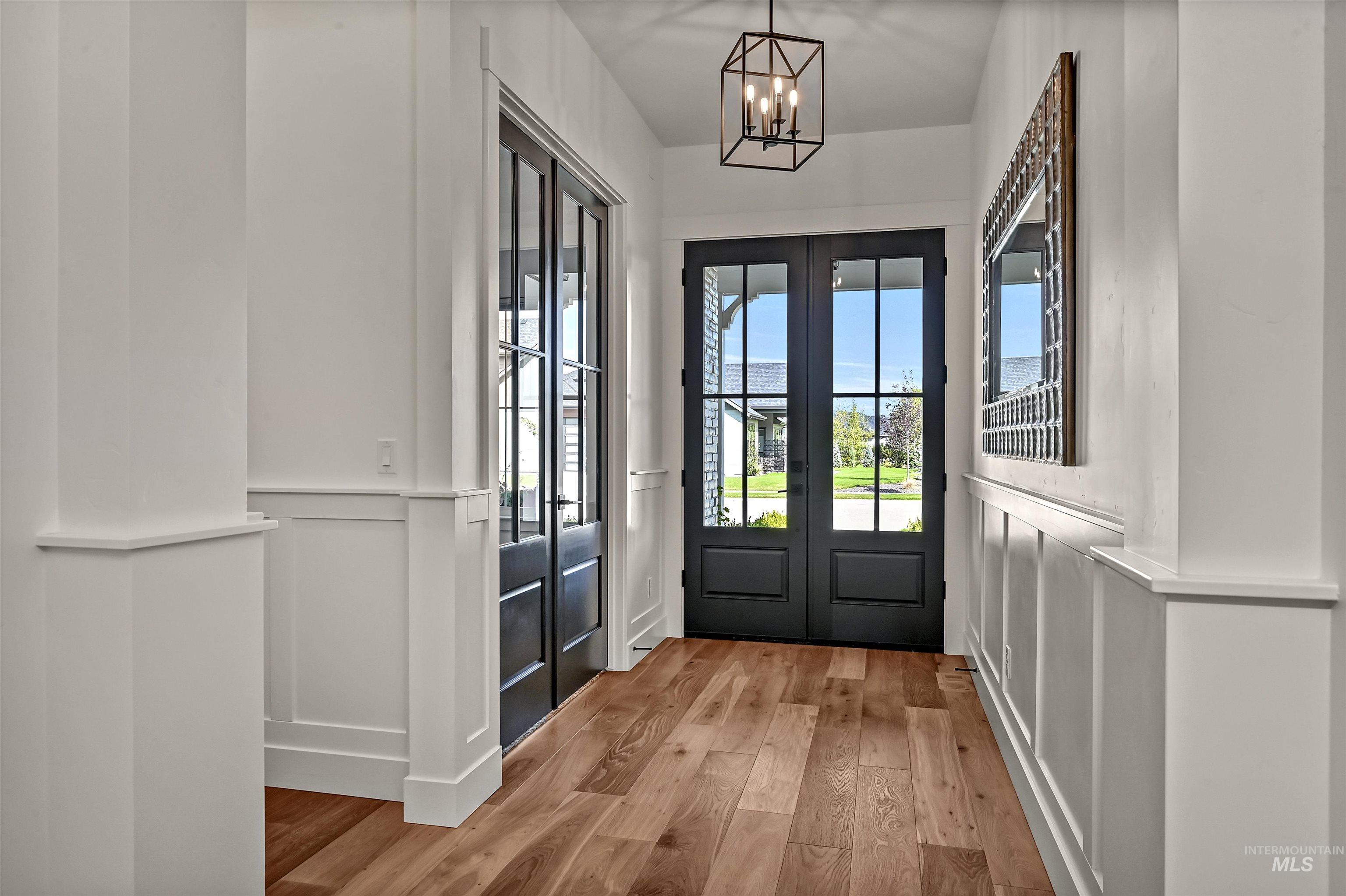 Doorway to outside featuring a decorative wall, french doors, wood finished floors, a chandelier, and a wainscoted wall