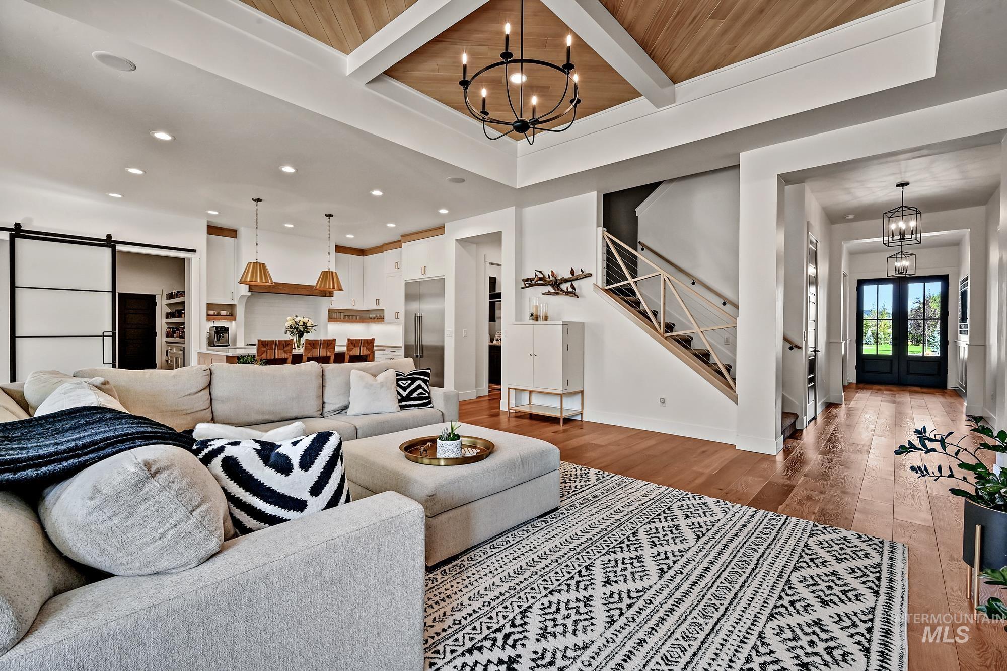 Living area with a chandelier, a barn door, light wood finished floors, stairway, and a wooden ceiling with exposed beams