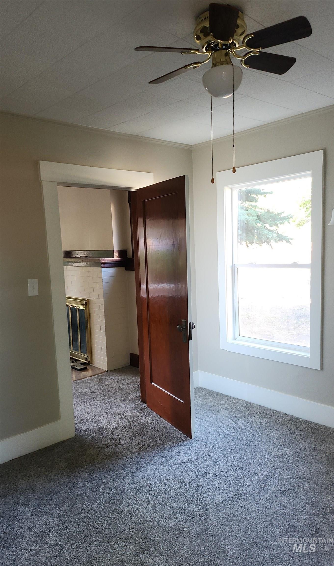 Unfurnished room with carpet, a ceiling fan, and a brick fireplace