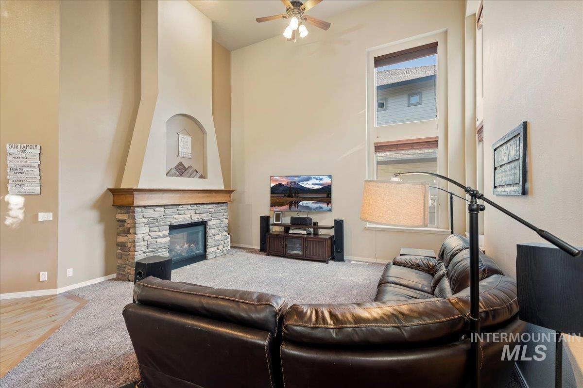Carpeted living area with a towering ceiling, a fireplace, and a ceiling fan