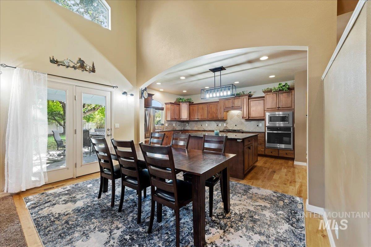 Dining room with light wood-style floors, recessed lighting, arched walkways, and a towering ceiling