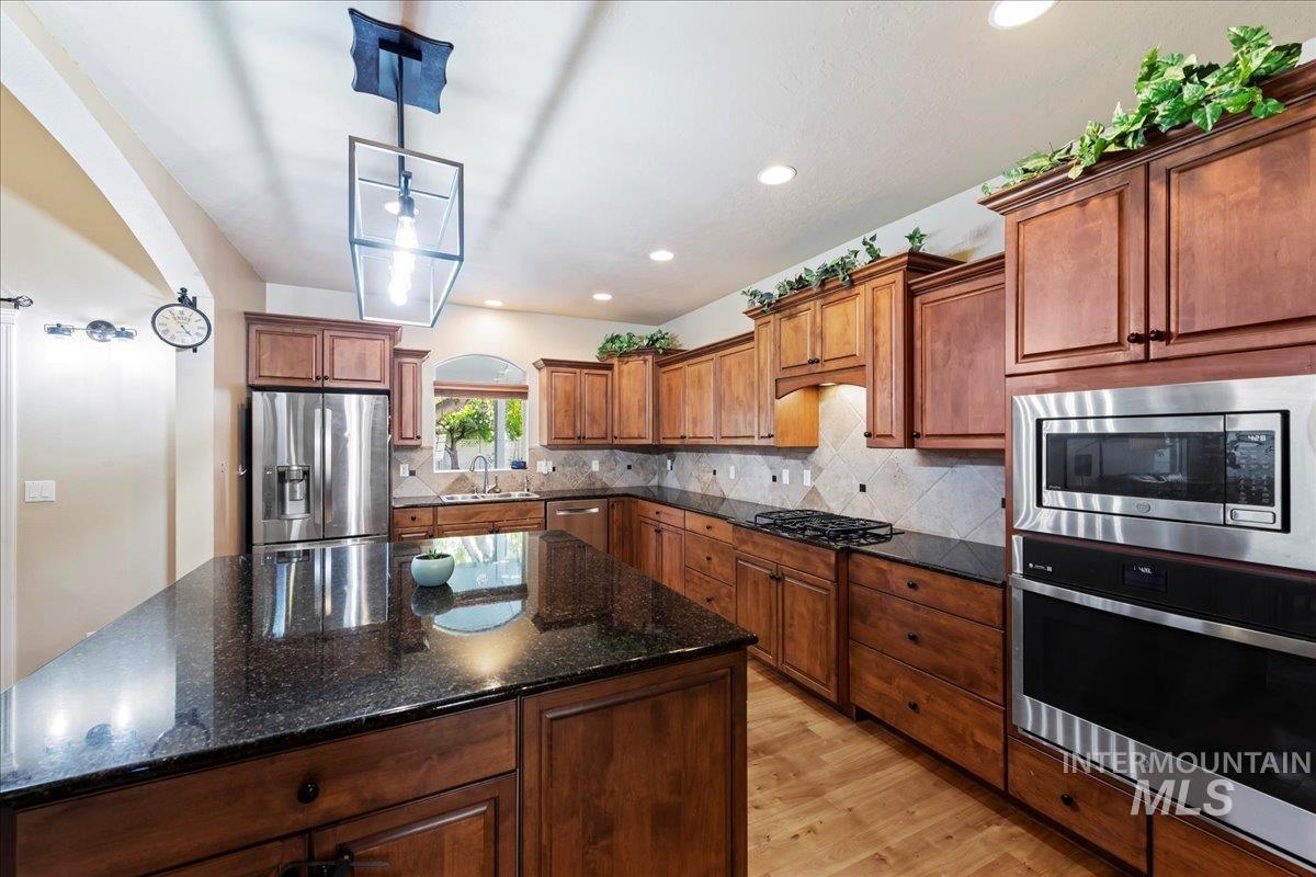 Kitchen with dark stone countertops, appliances with stainless steel finishes, light wood-style flooring, tasteful backsplash, and recessed lighting