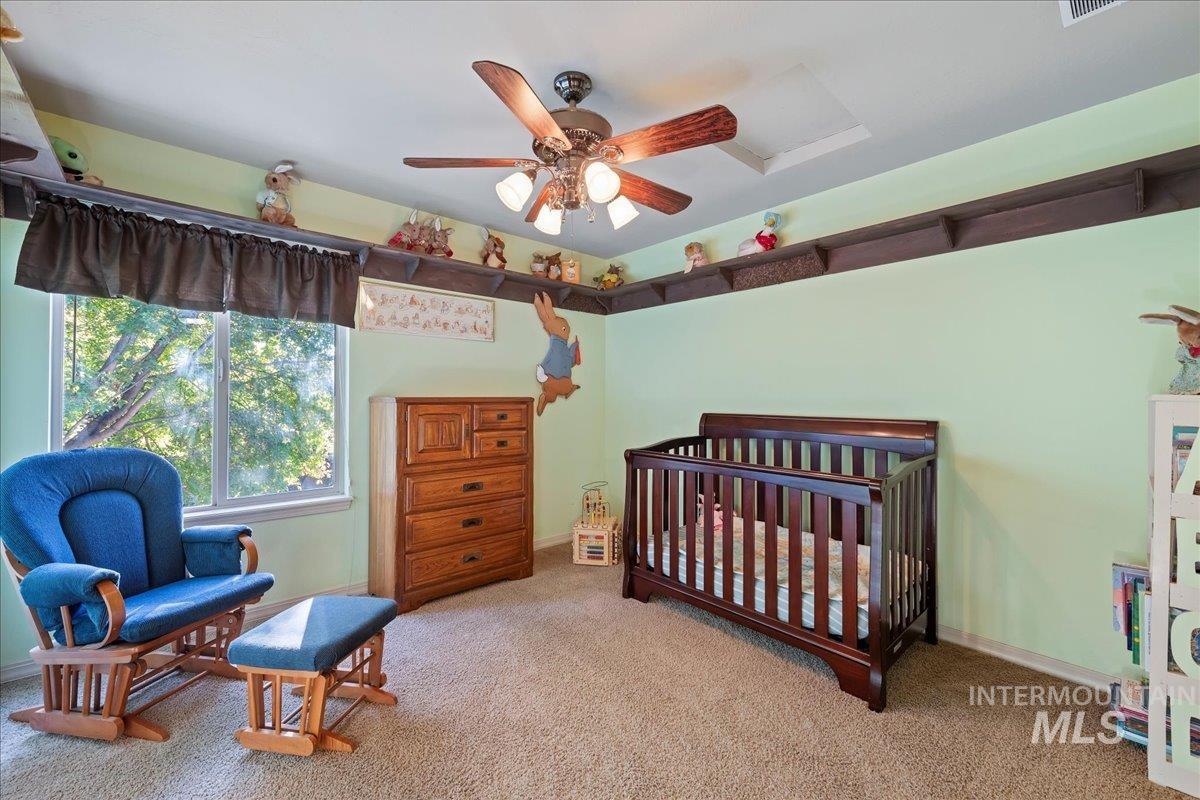 Carpeted bedroom featuring a crib, attic access, and ceiling fan